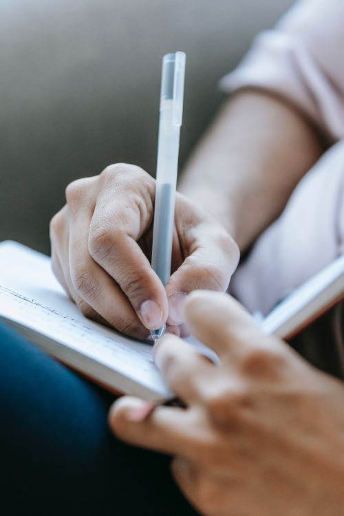 person holding pen and writing in a notebook