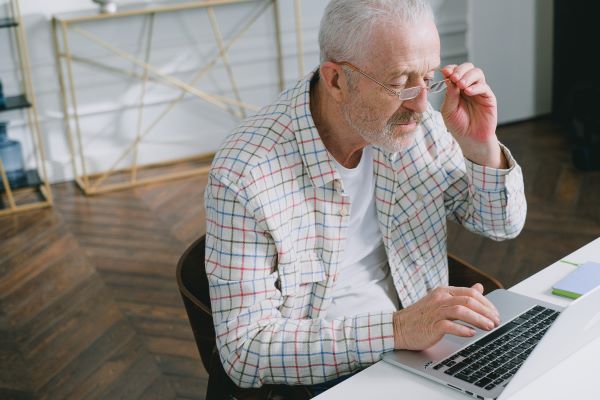 man sitting at desk, looking at his computer and adjusting his glasses